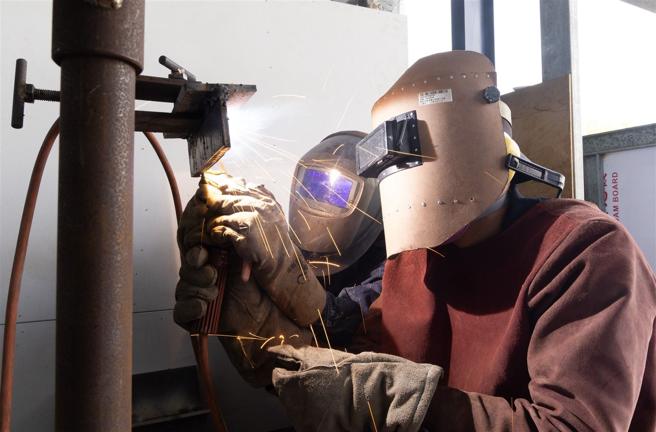 教官带着学员操作「仰角銲」姿势，让学员可以更清楚了解銲接技巧与标准。（记者尤韵婷摄）