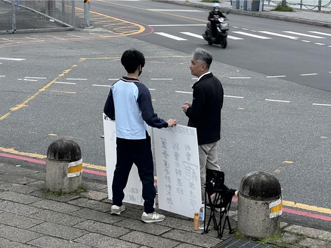 花莲花岗国中有名男校友，今天傍晚穿着校服，站在校门口声援叶春莲，校方虽尊重个人言论自由，但认为穿着校服就代表学校，便上前了解、关心。（罗亦晽摄）
