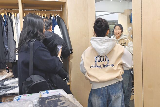 韓國各大學向來有訂製棒球外套的傳統，早就是流行象徵。圖為首爾大學紀念品店內，學生正在試穿棒球外套。（黃琮淵攝）