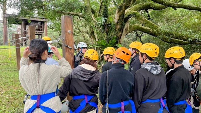 學員們穿戴安全吊帶與防護頭盔，聚精會神地聆聽教練的說明，確保在挑戰高空繩索時能夠熟悉安全規範與操作技巧。(照片/聖約翰科大提供)
