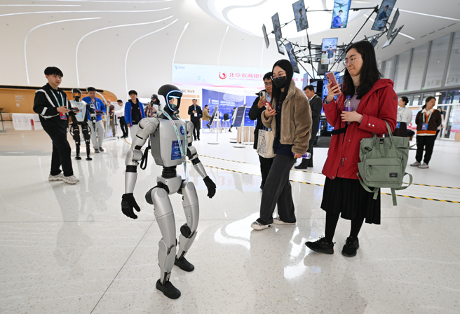 随着人工智慧（AI）人形机器人进展迅速，近来在大陆上各商业场所成为热门宠儿，经营机器人租赁生意也为热门行业。图为展场上行走的宇树G1机器人吸引人们拍照。（图／新华社）