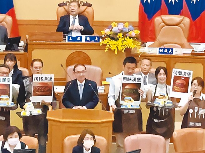 民进党议员10日市政总质询响应新北市长侯友宜（站备询台者）先前赴美称「失业卖汉堡」一说，端出象徵国民党主席朱立伦和下届市长热门人选的「烤猪汉堡」、「葱味汉堡」、「四川汉堡」、「荷兰汉堡」要侯友宜选，侯笑回「怎么这么关心国民党、民眾党的事情勒，关心市政才是关心新北市」。（柯毓庭摄）