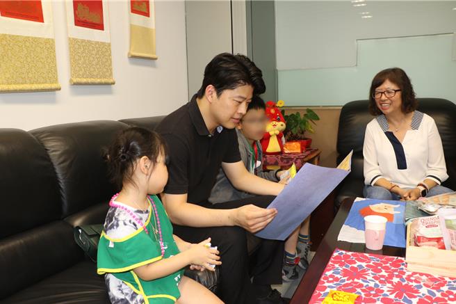 前太平獅子會會長陳書玄帶著小孩來捐助10萬元獎學金 他閱讀千千寫給他的大卡片。（新北市社會局提供）