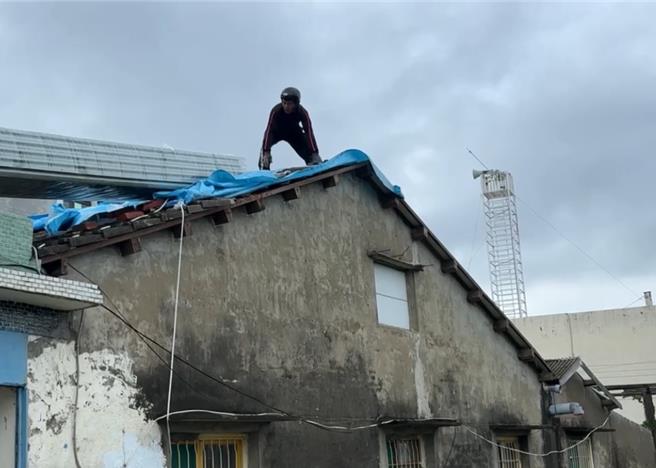 屋頂帆頂被吹翻的受災戶，天氣放晴後忙著上屋頂重蓋帆布。（郭良傑攝）
