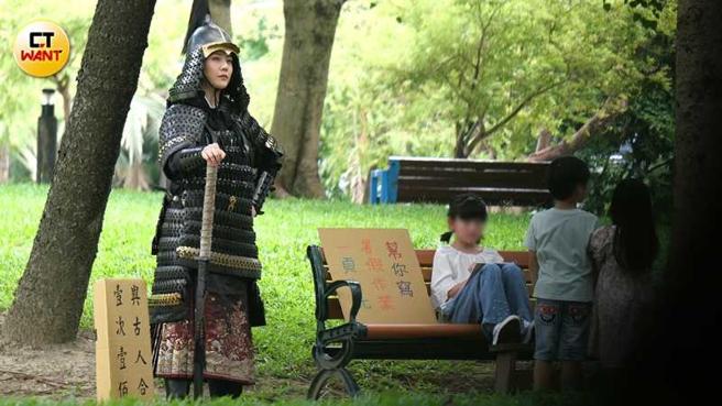 武将装扮的韩瑜手握长刀喊着「与古人合照一次一百」，而坐在椅子上的小女孩身边纸牌写着「帮你写暑假作业一页十元」，画面相当好笑。（图／本刊摄影组）