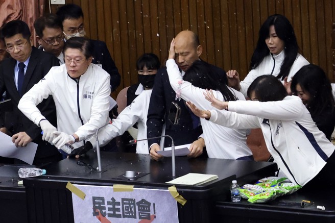 2024年12月20日立法院會20日排審選罷法等案，立法院長韓國瑜（上排中）約於11時50分在國民黨立委護送下站上主席台，宣布採舉手表決，遭到民進黨立委邱議瑩潑水。 （資料照／鄧博仁攝）

