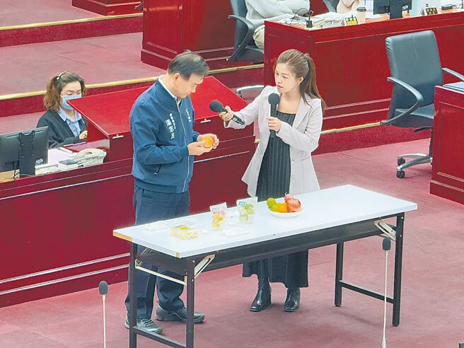 台北市学校营养午餐会提供水果，不过，学童享用芭乐、百香果时必须靠刀具截切才有办法吃，市议员洪婉臻（右）11日在议会教育部门质询，请北市教育局长汤志民（左）体验学生食用的难处。（张珈瑄摄）