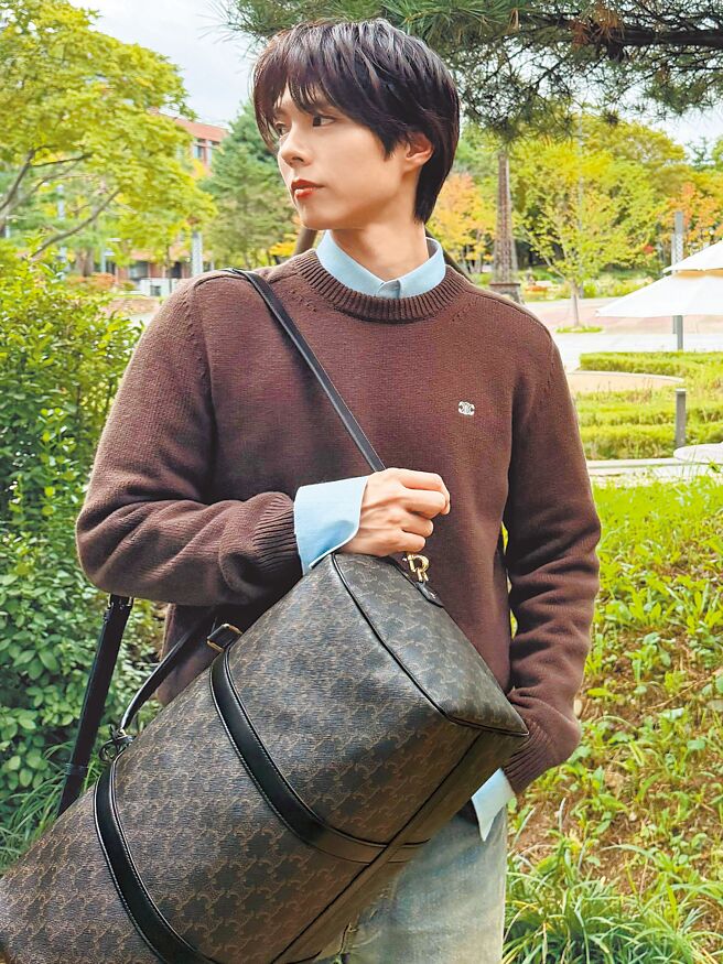 朴宝剑以棕色针织上衣层迭淡蓝衬衫，肩背CELINE标志印花旅行袋，流露自然率性的旅程姿态。（CELINE提供）