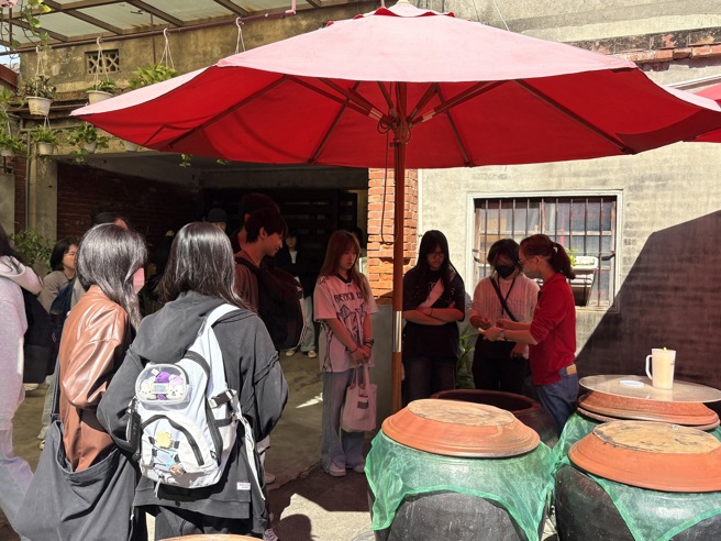 南華大學學生至「丸莊醬油」參訪，學生們品嚐發酵缸中的醬油，味道更濃郁甘醇。(南華大學提供)