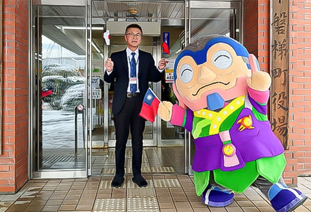福島縣磐梯町產業振興課商工觀光係長遠藤哲熱情歡迎台灣旅客造訪盤梯町。旁邊是磐梯町吉祥物「ロボばんじい(Robo Banji)」。(攝影＝廖苡安)